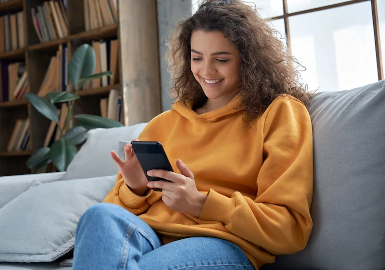 young woman using phone and sitting on couch