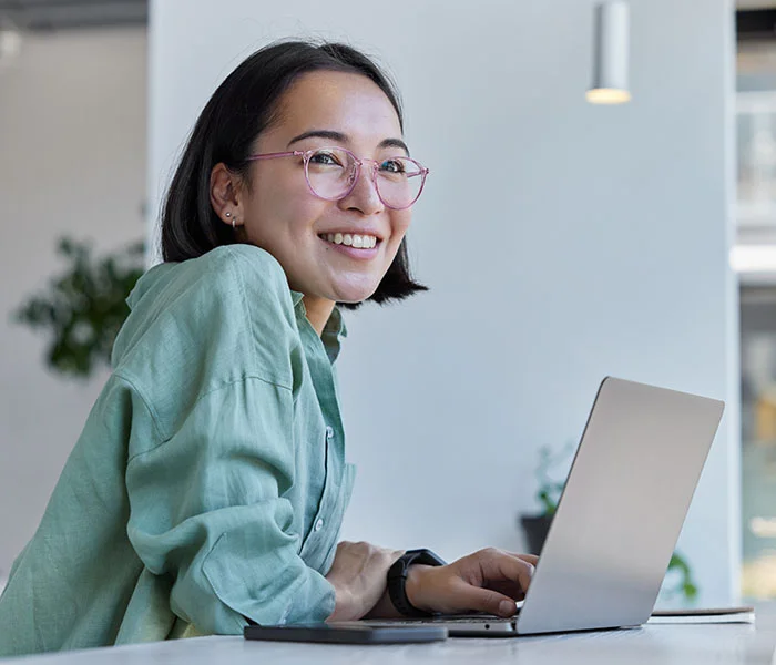 Asian woman in eyeglasses and casual clothes browses laptop computer